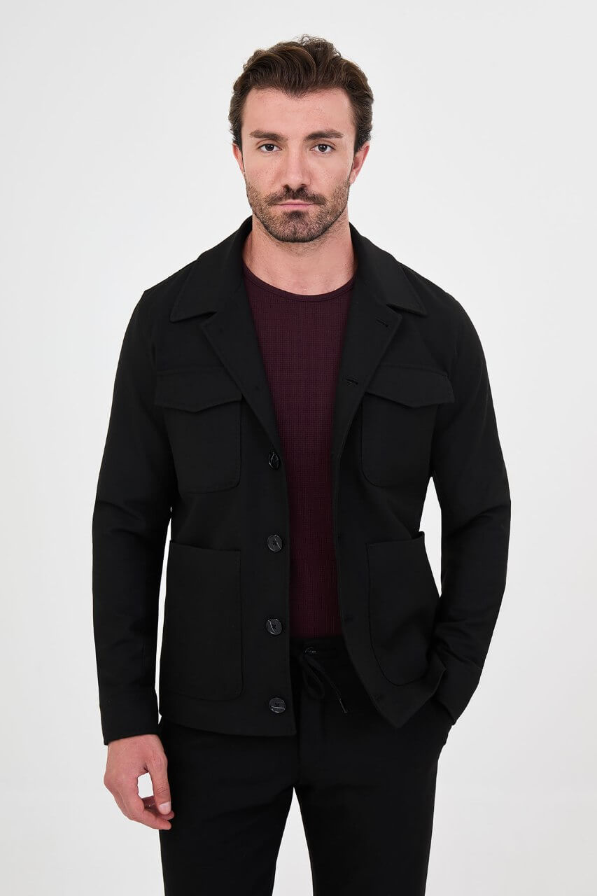 Men's black fall/winter utility jacket styled with a burgundy crew-neck shirt and black trousers.