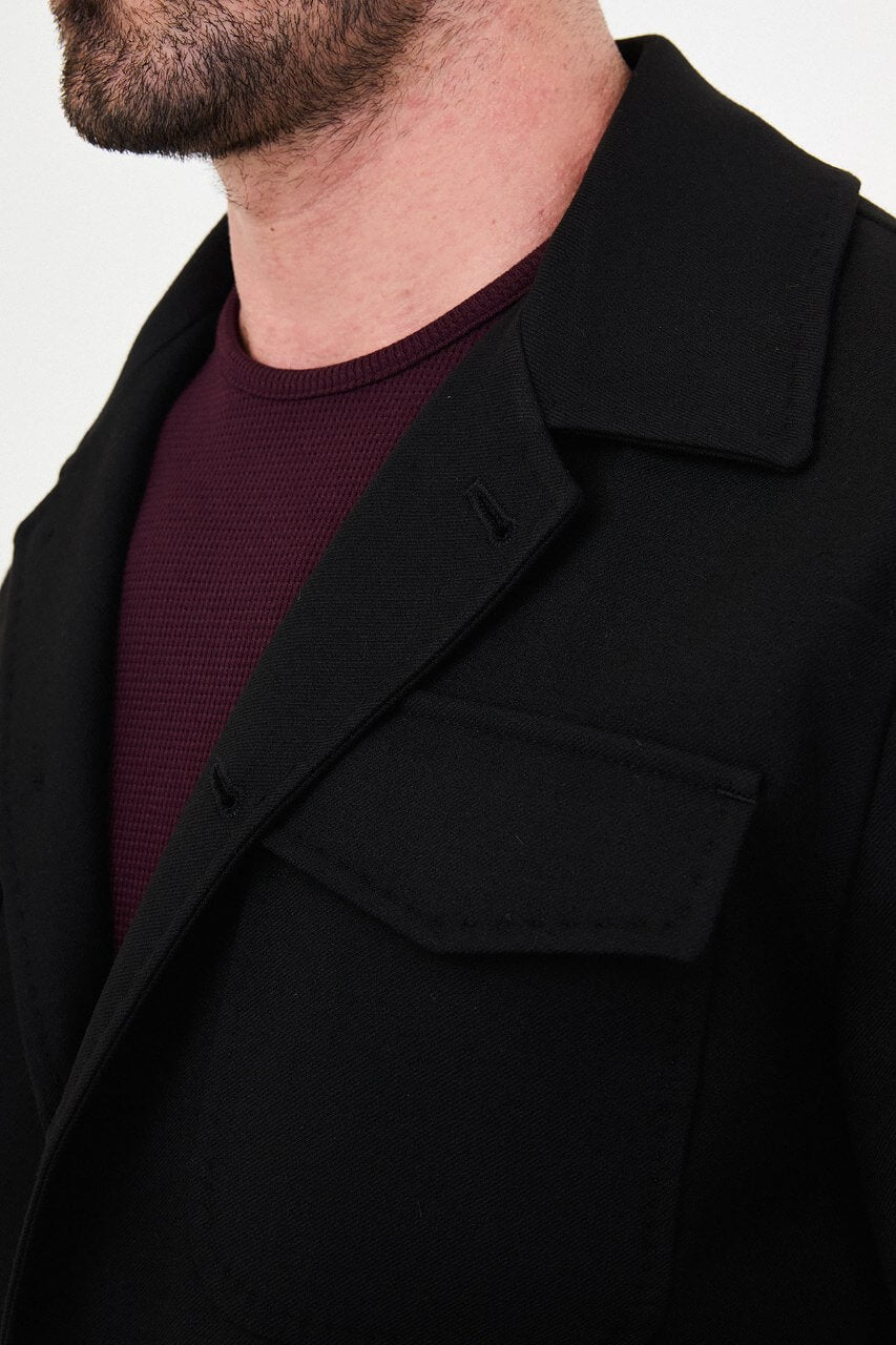 Men's black fall/winter utility jacket styled with a burgundy crew-neck shirt and black trousers.