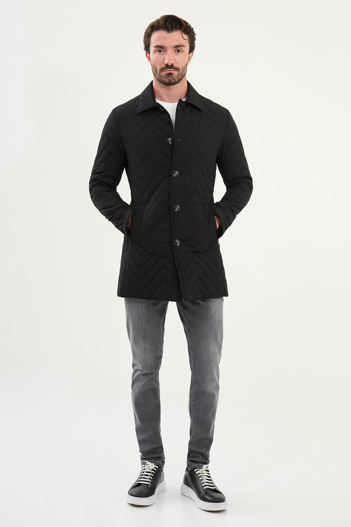 Full-body view of model wearing men's black quilted car coat styled with grey jeans and sneakers.