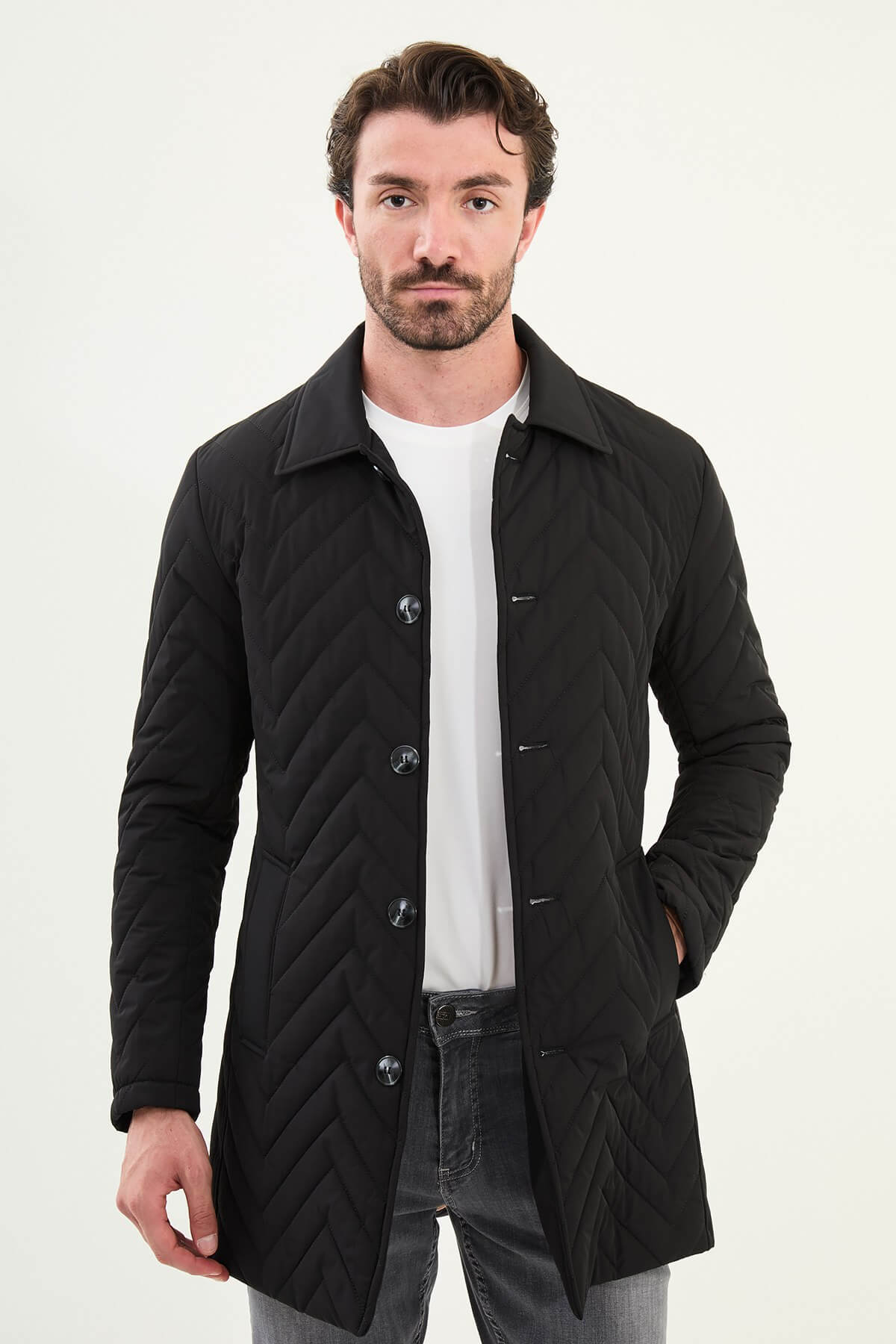 Full-body view of model wearing men's black quilted car coat styled with grey jeans and sneakers.