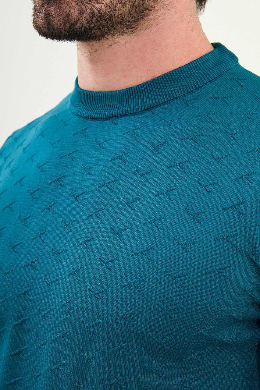 Men’s teal-blue slim-fit crew-neck sweater with geometric ‘T’ textured knit front panel, cotton-viscose-elastane blend, styled with white trousers.