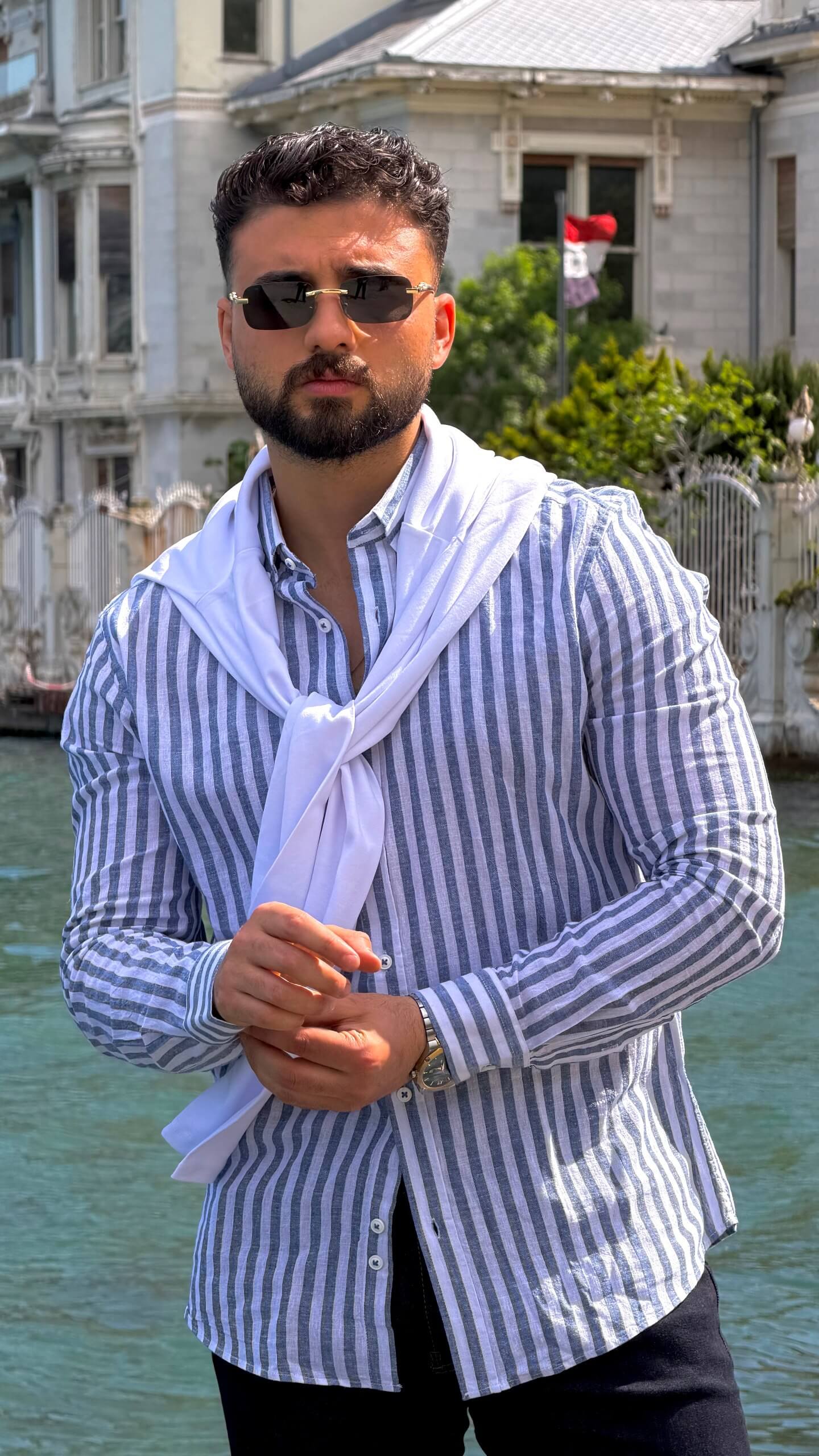 Man wearing navy blue vertical-striped oversize linen-cotton blend shirt with rolled-up sleeves by the water