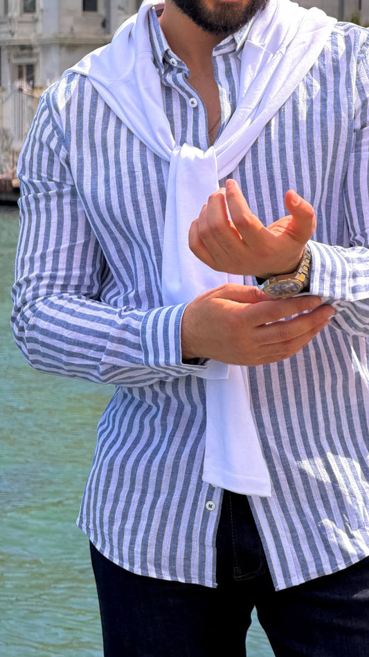 Man wearing navy blue vertical-striped oversize linen-cotton blend shirt with rolled-up sleeves by the water