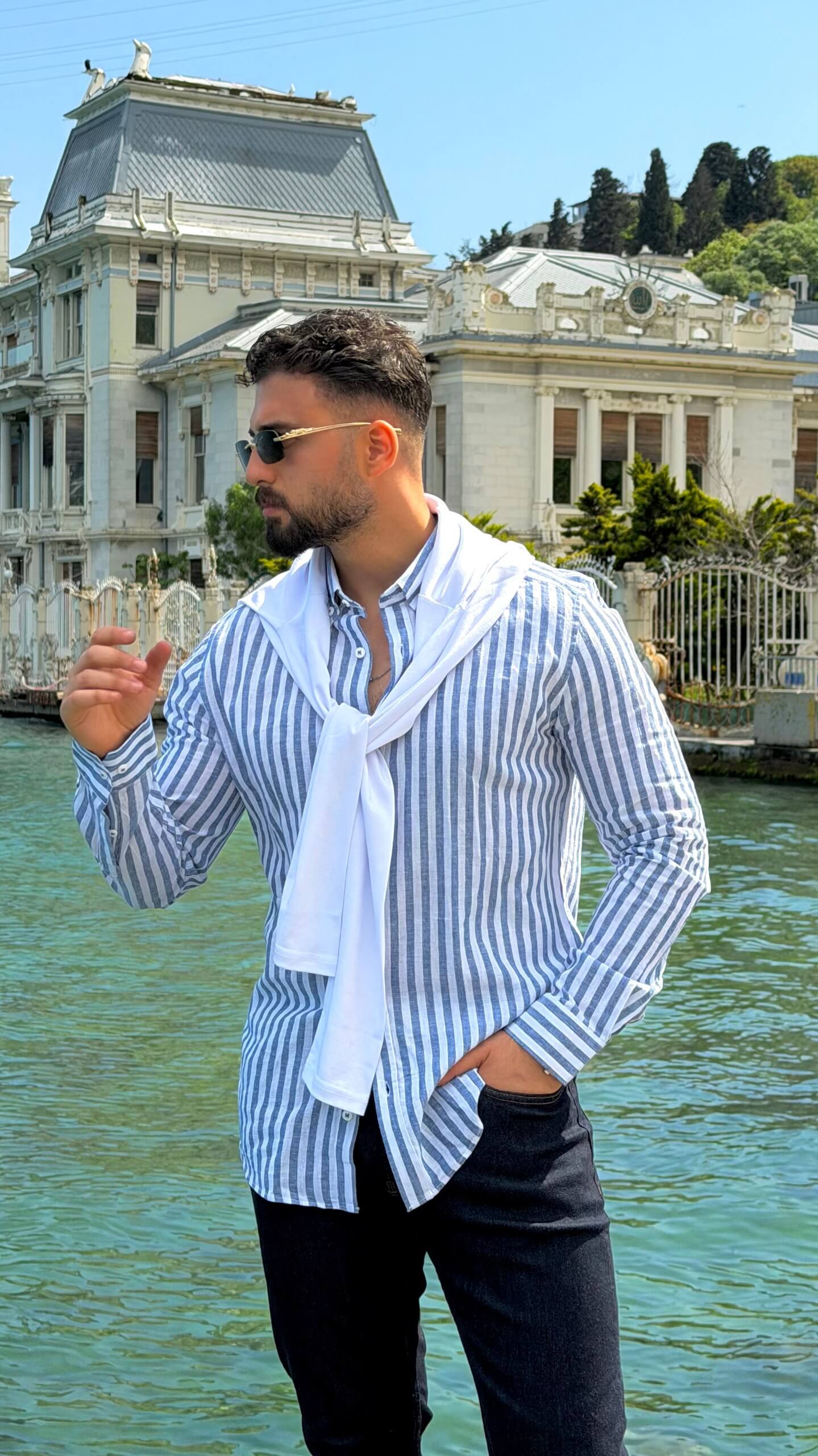 Man wearing navy blue vertical-striped oversize linen-cotton blend shirt with rolled-up sleeves by the water
