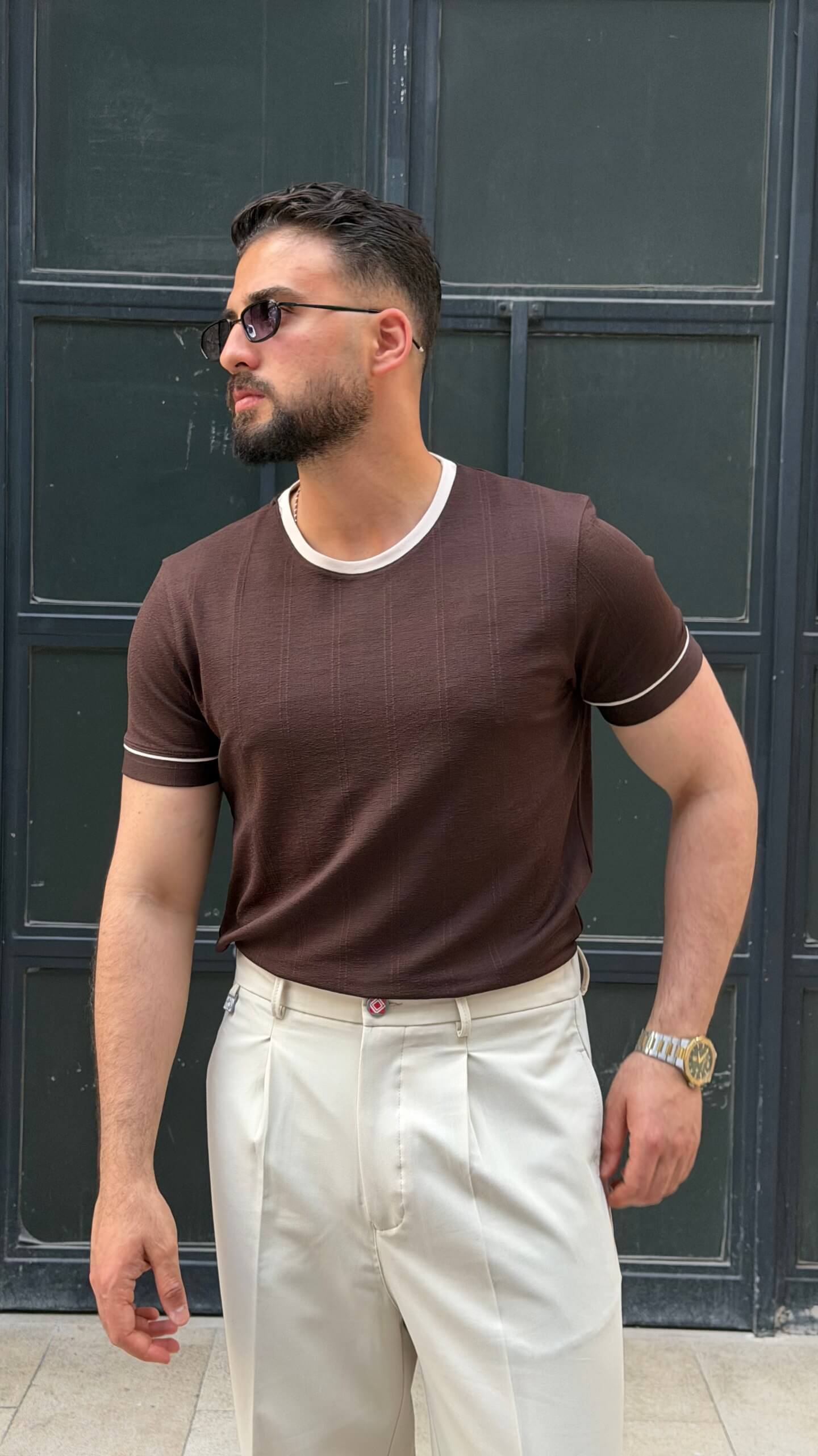 brown crew neck T-shirt with subtle texture, worn by a male model, paired with cream trousers, showcasing a slim fit and short sleeves.