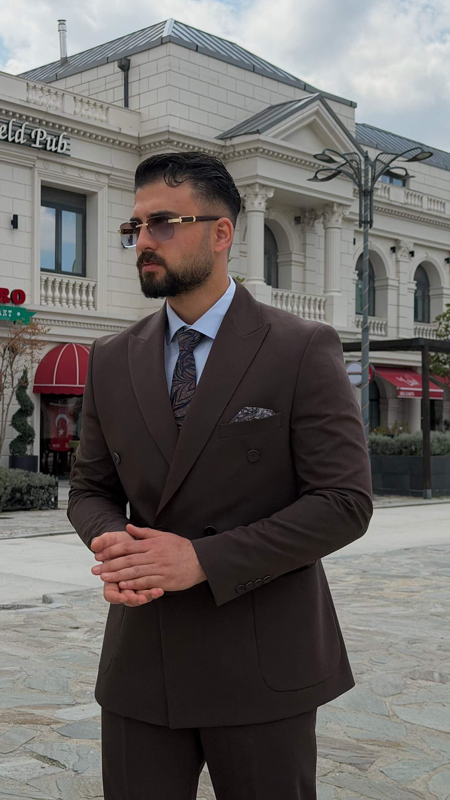 Men wearing a brown double-breasted slim-fit two-piece suit standing outdoors, styled with black shoes and a tie.