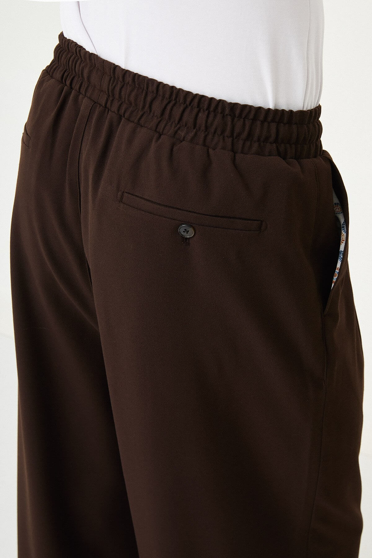 Men wearing brown luxe drawstring jersey pants with white sneakers, styled for a smart-casual summer look.