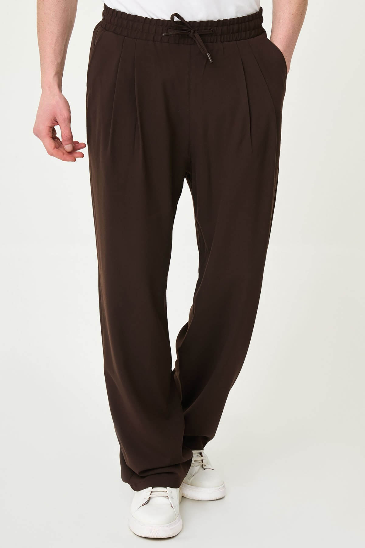 Men wearing brown luxe drawstring jersey pants with white sneakers, styled for a smart-casual summer look.