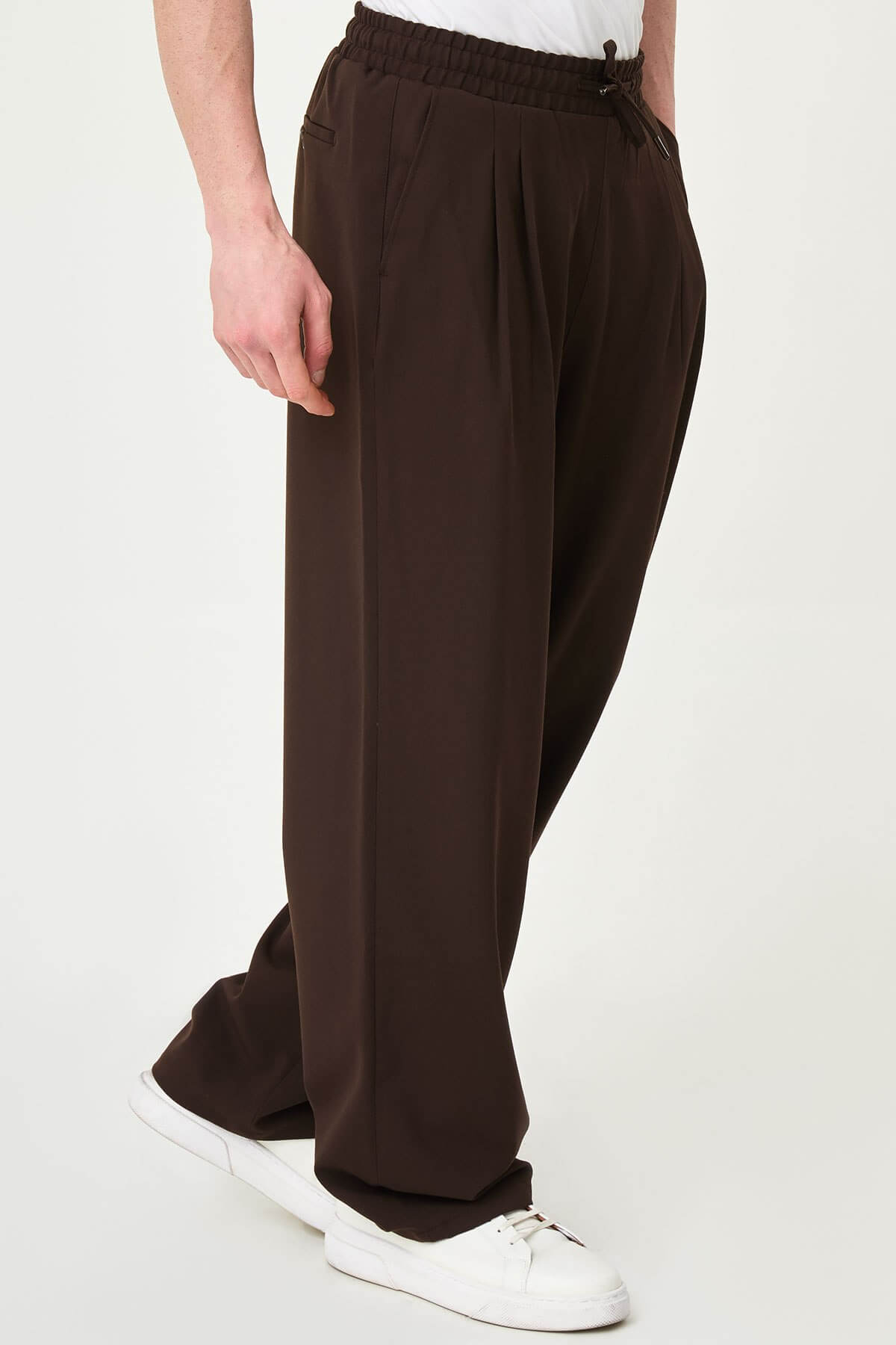 Men wearing brown luxe drawstring jersey pants with white sneakers, styled for a smart-casual summer look.