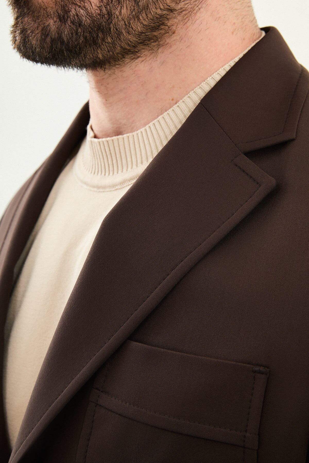 Men’s brown slim fit blazer with a clean modern design and stretch fabric, styled with a beige knit top for elegant smart casual and evening looks.