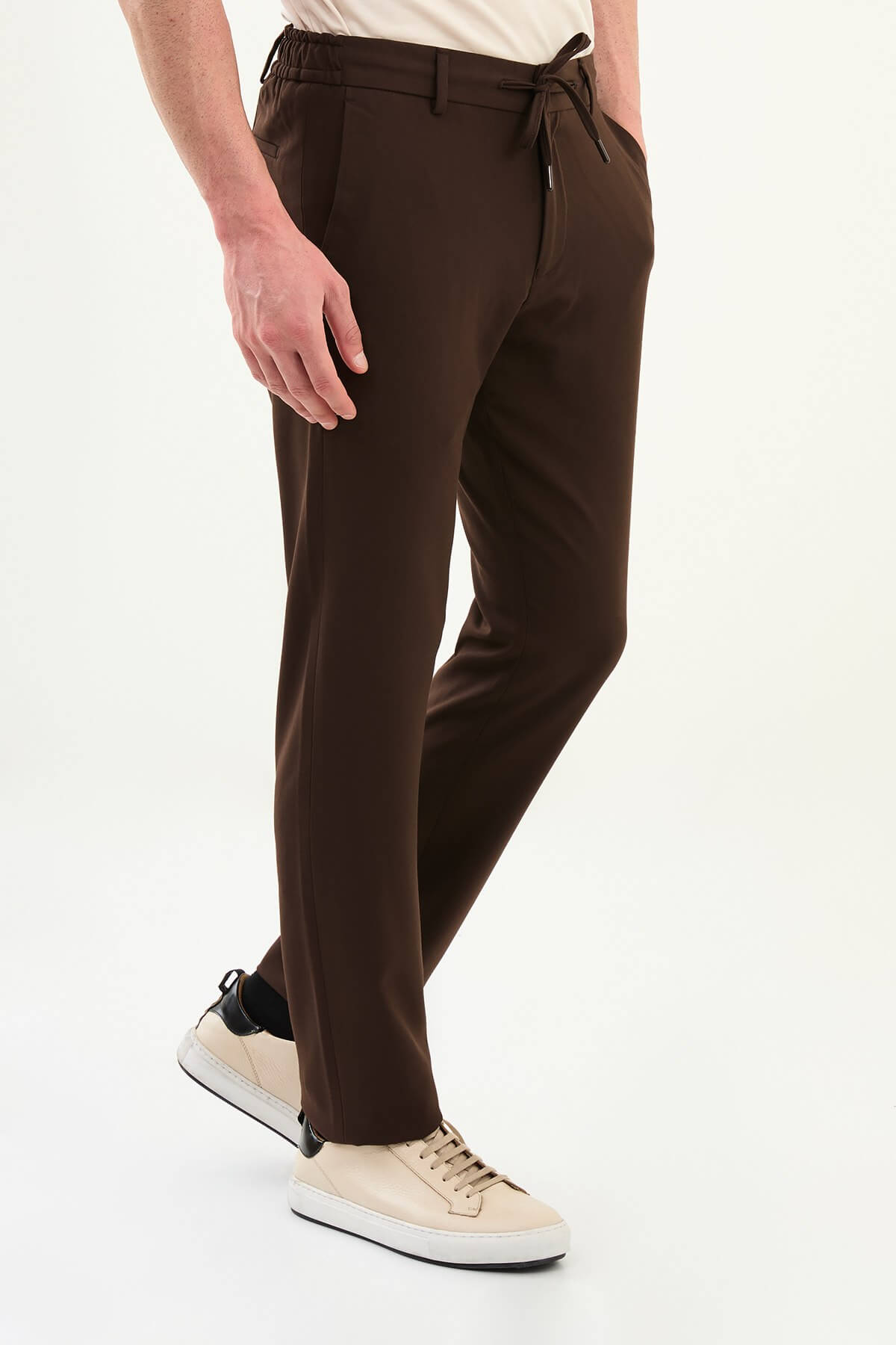 Men wearing brown slim-fit drawstring trousers with elastic waistband, tapered slim fit, styled with sneakers and dress shoes for versatile summer menswear.