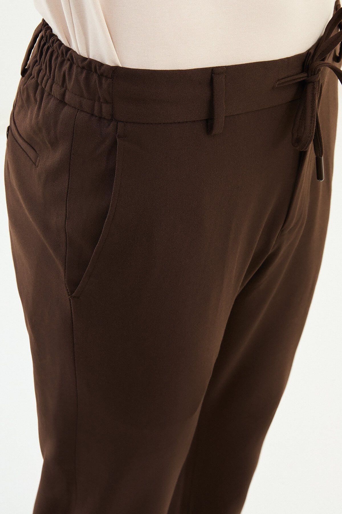 Men wearing brown slim-fit drawstring trousers with elastic waistband, tapered slim fit, styled with sneakers and dress shoes for versatile summer menswear.