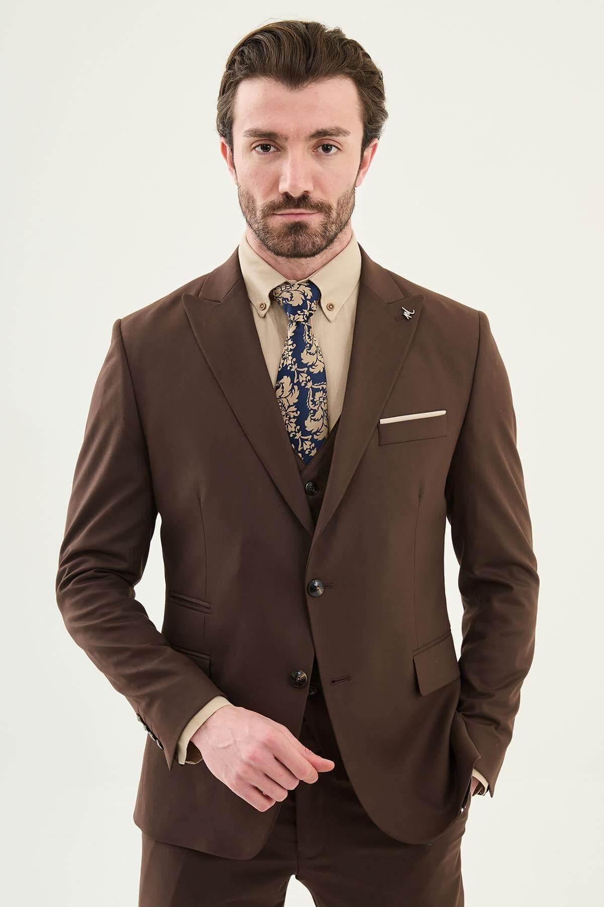 Man wearing a brown three-piece suit with blazer, waistcoat, and trousers, paired with a beige shirt and patterned tie