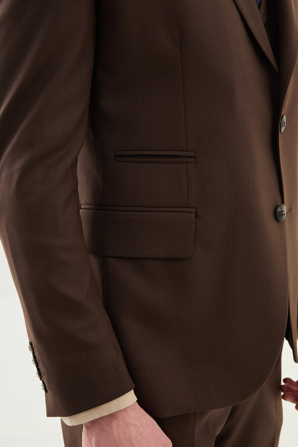 Man wearing a brown three-piece suit with blazer, waistcoat, and trousers, paired with a beige shirt and patterned tie