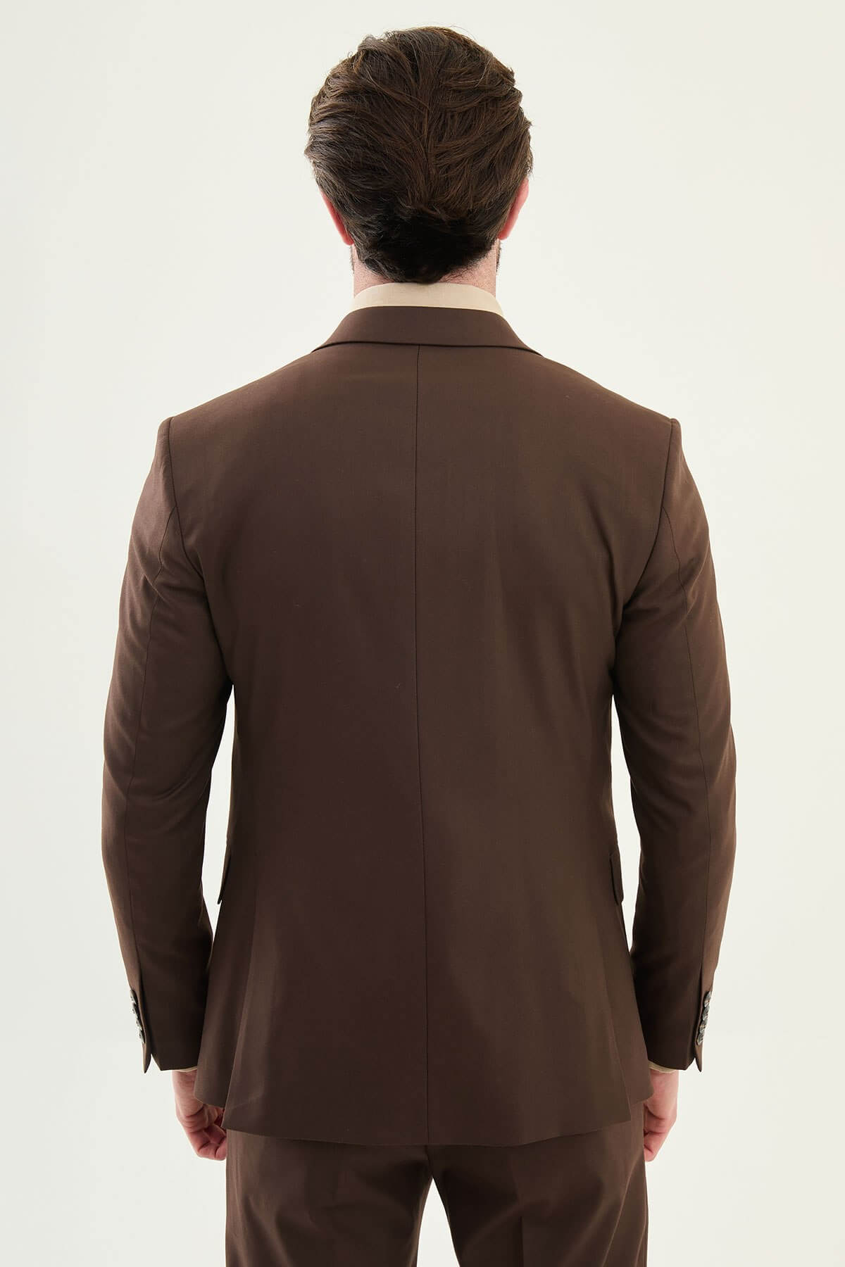 Man wearing a brown three-piece suit with blazer, waistcoat, and trousers, paired with a beige shirt and patterned tie