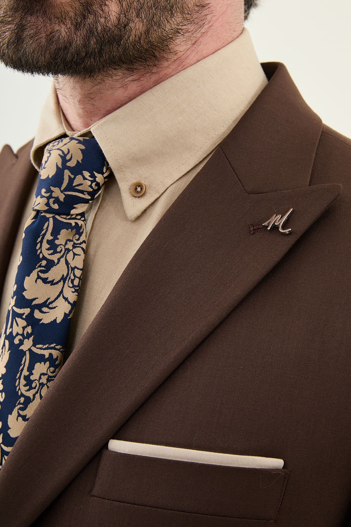 Man wearing a brown three-piece suit with blazer, waistcoat, and trousers, paired with a beige shirt and patterned tie