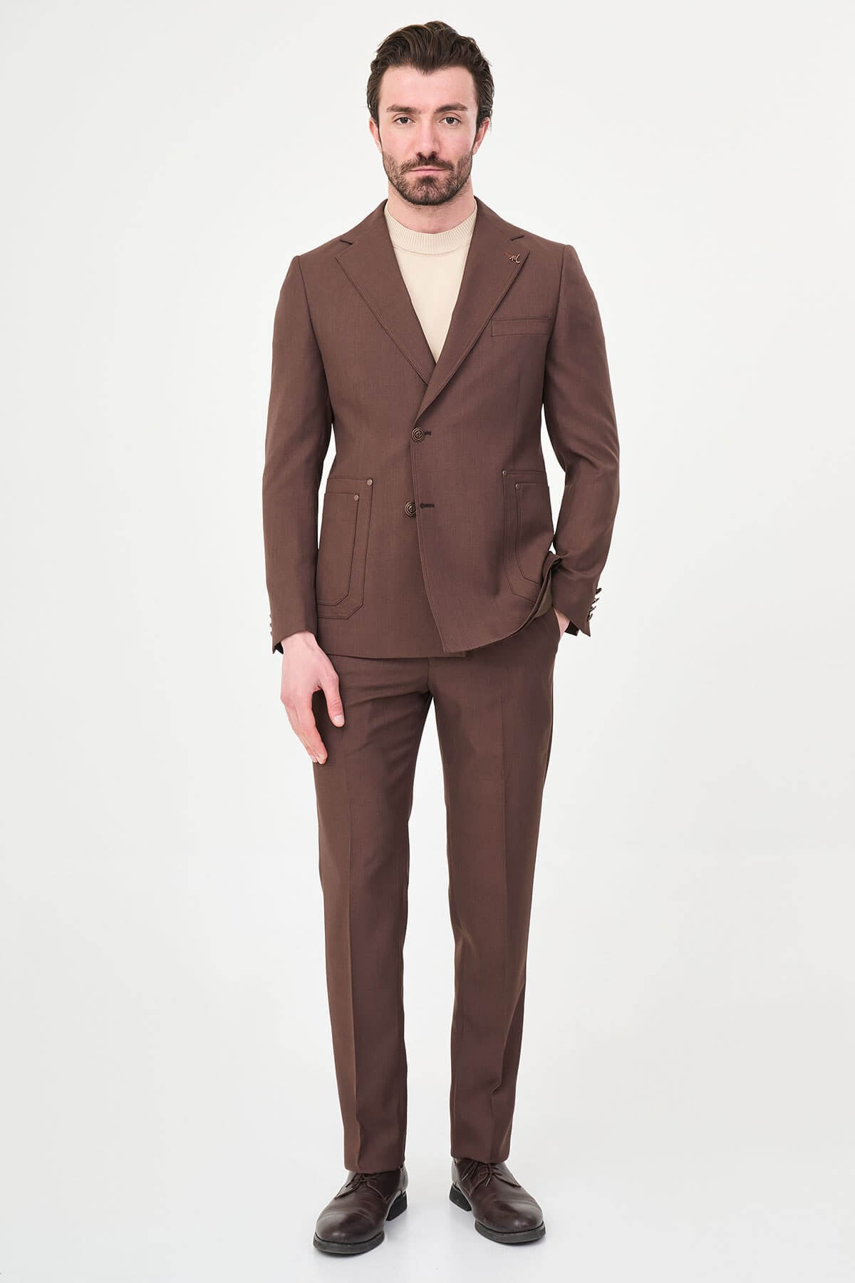 a brown slim-fit two-piece wedding suit with notch lapels, utility-style stitched lower pockets, cream knitwear, matching tailored trousers, and dark brown leather shoes.