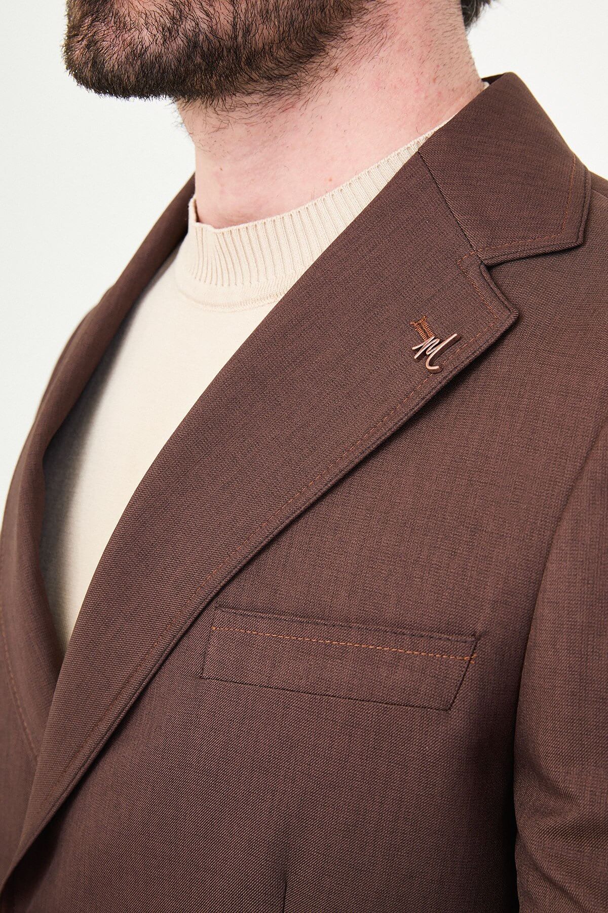 a brown slim-fit two-piece wedding suit with notch lapels, utility-style stitched lower pockets, cream knitwear, matching tailored trousers, and dark brown leather shoes.