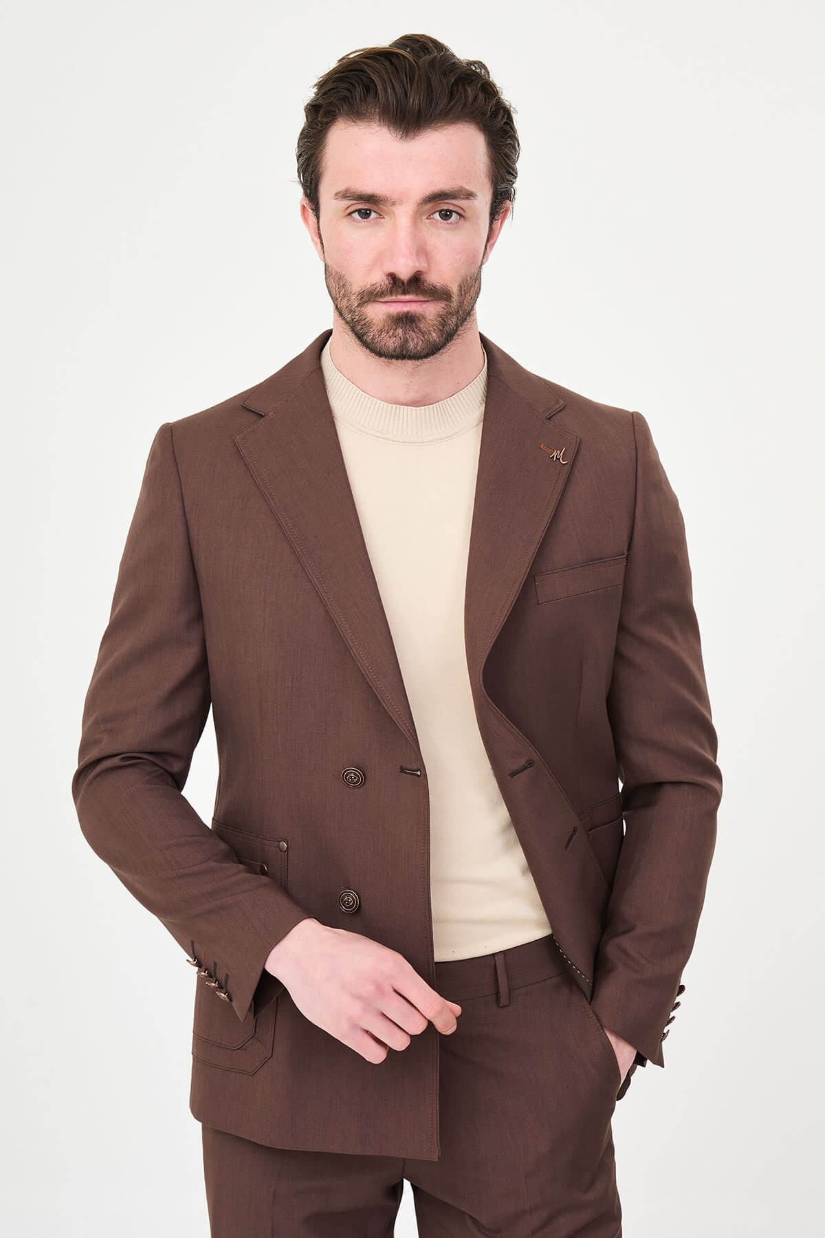 a brown slim-fit two-piece wedding suit with notch lapels, utility-style stitched lower pockets, cream knitwear, matching tailored trousers, and dark brown leather shoes.