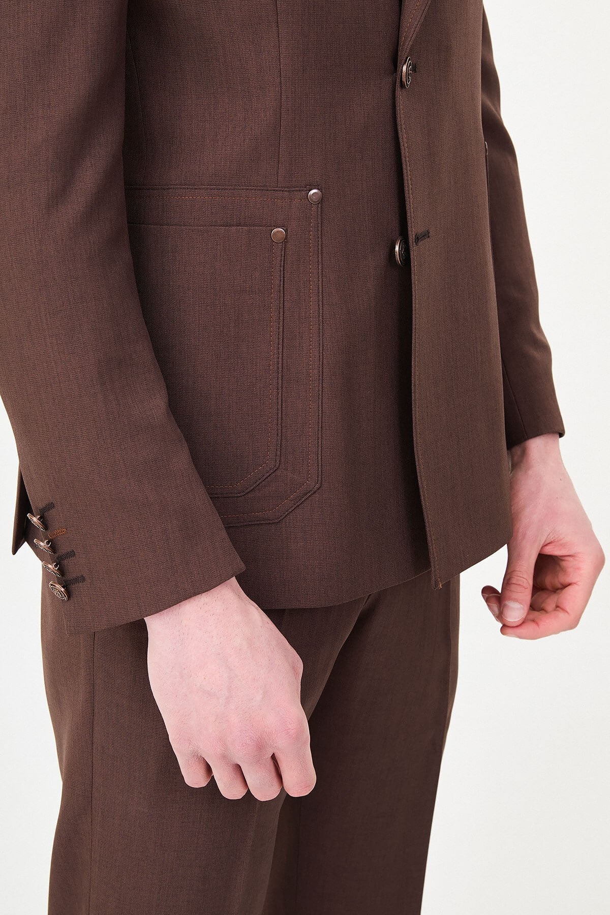 a brown slim-fit two-piece wedding suit with notch lapels, utility-style stitched lower pockets, cream knitwear, matching tailored trousers, and dark brown leather shoes.
