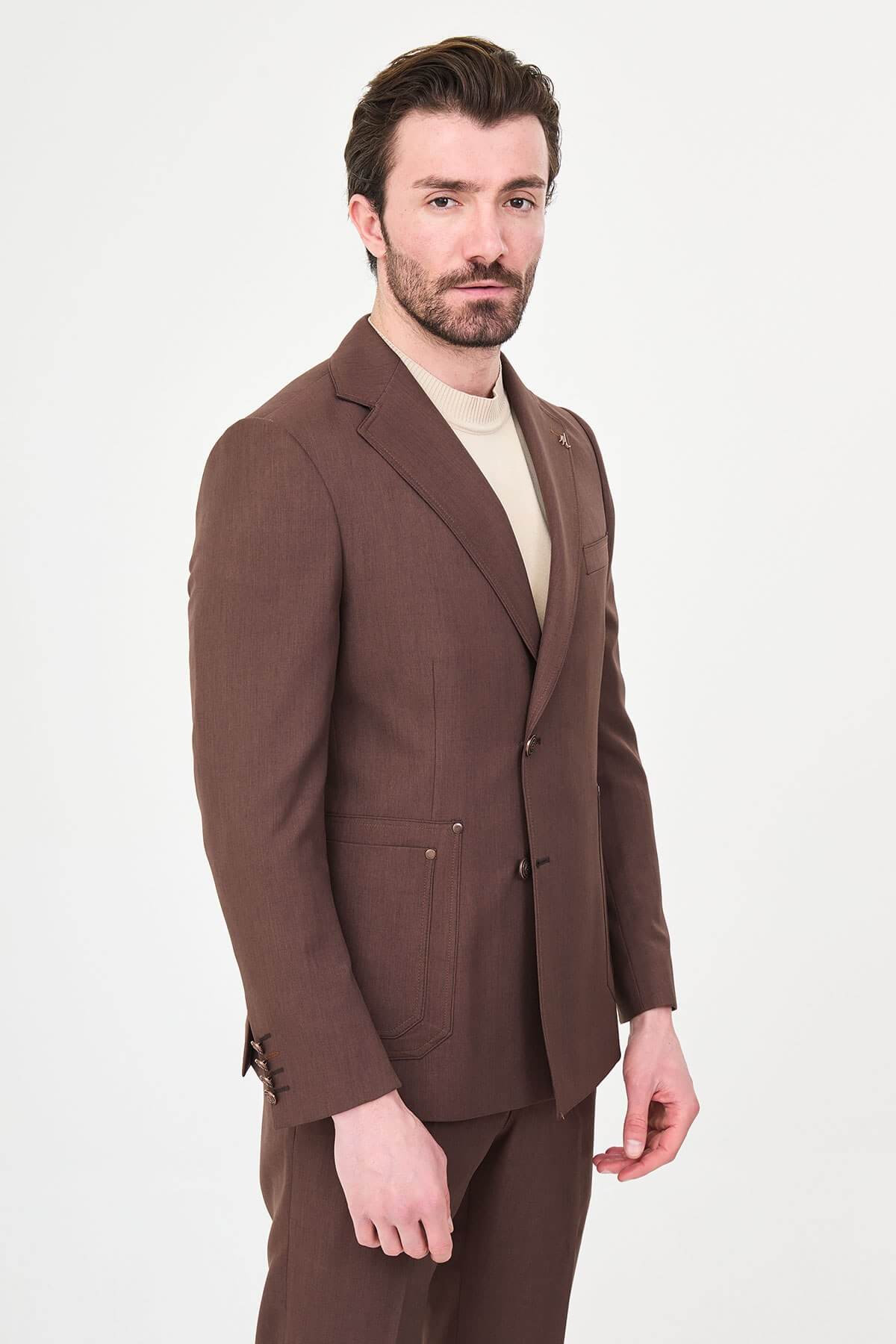 a brown slim-fit two-piece wedding suit with notch lapels, utility-style stitched lower pockets, cream knitwear, matching tailored trousers, and dark brown leather shoes.