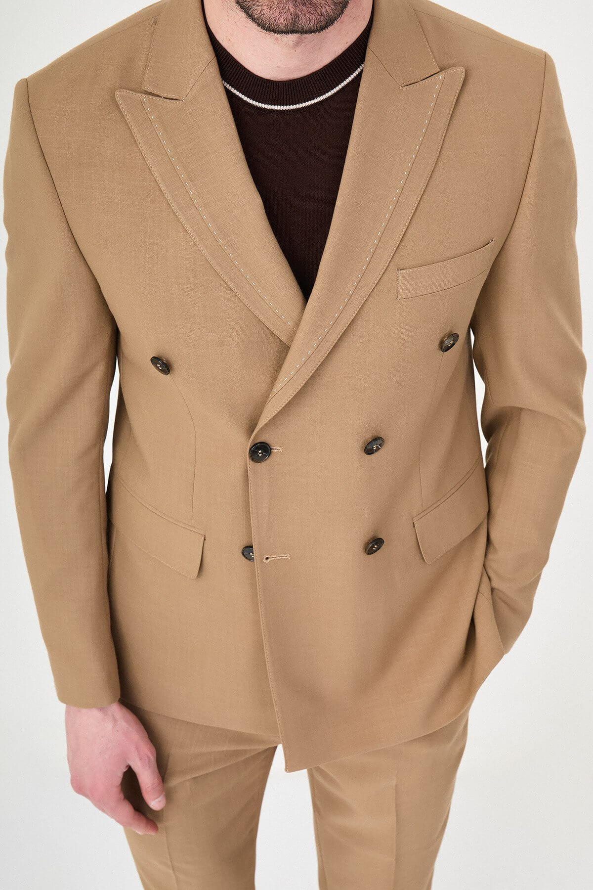 a camel slim-fit double-breasted linen-blend suit with peak lapels, dark buttons, matching trousers, a dark brown knit polo, and brown leather sneakers.