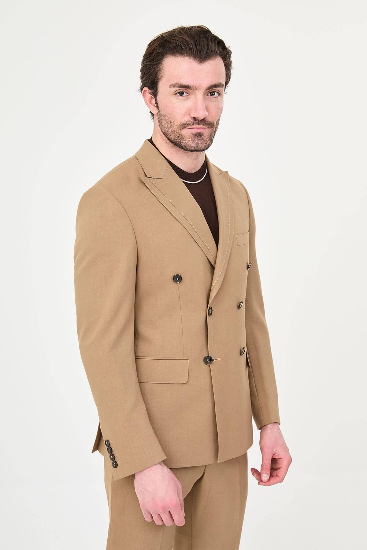 a camel slim-fit double-breasted linen-blend suit with peak lapels, dark buttons, matching trousers, a dark brown knit polo, and brown leather sneakers.