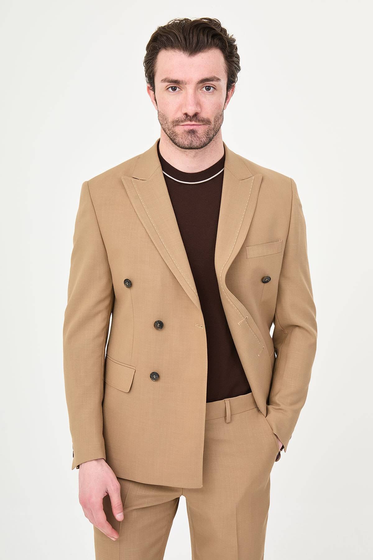 a camel slim-fit double-breasted linen-blend suit with peak lapels, dark buttons, matching trousers, a dark brown knit polo, and brown leather sneakers.