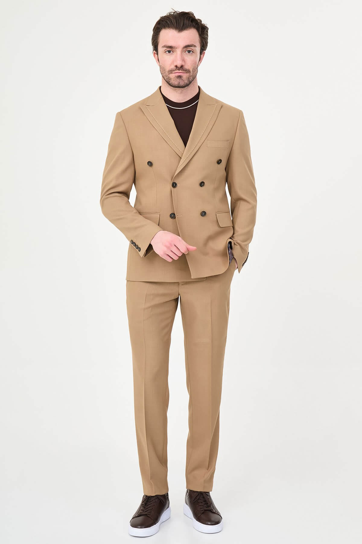 a camel slim-fit double-breasted linen-blend suit with peak lapels, dark buttons, matching trousers, a dark brown knit polo, and brown leather sneakers.