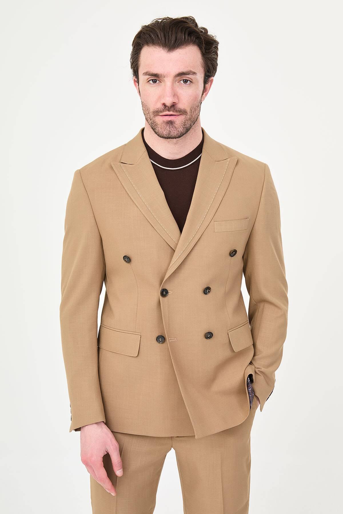 a camel slim-fit double-breasted linen-blend suit with peak lapels, dark buttons, matching trousers, a dark brown knit polo, and brown leather sneakers.