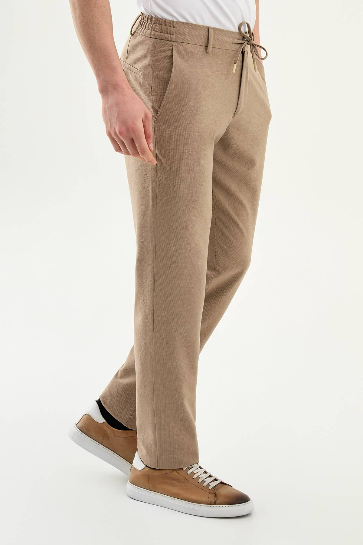 Man wearing camel slim-fit summer trousers paired with a white polo shirt and casual sneakers.