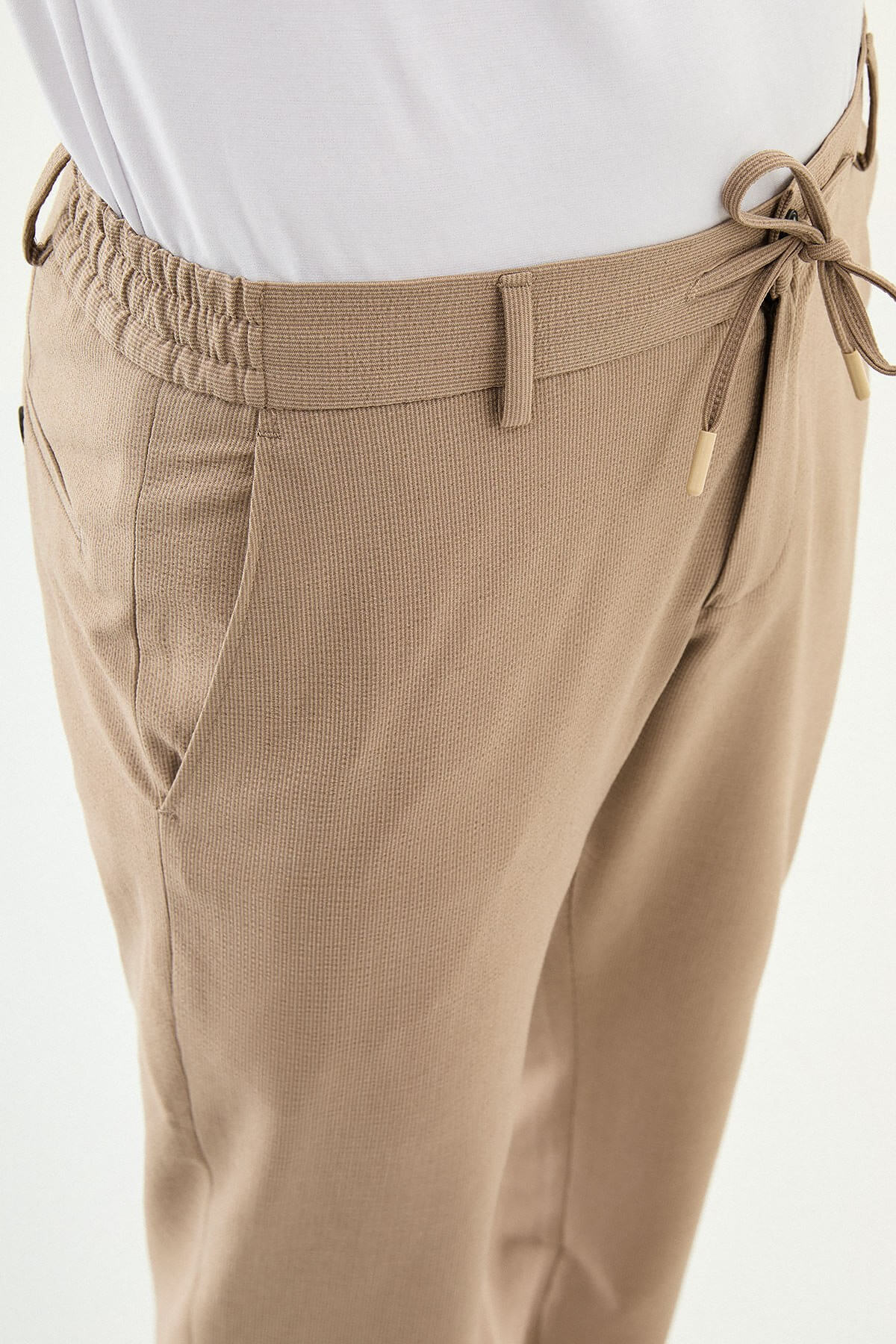 Man wearing camel slim-fit summer trousers paired with a white polo shirt and casual sneakers.