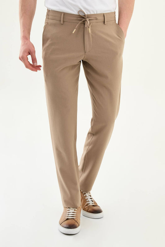 Man wearing camel slim-fit summer trousers paired with a white polo shirt and casual sneakers.