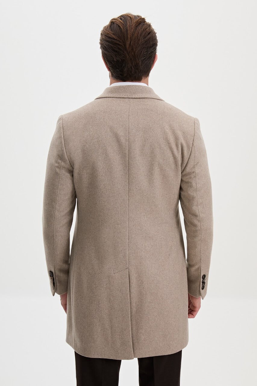 Men's beige single-breasted winter coat styled with a black sweater, dark trousers, and brown leather boots.