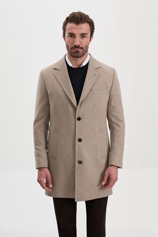 Men's beige single-breasted winter coat styled with a black sweater, dark trousers, and brown leather boots.