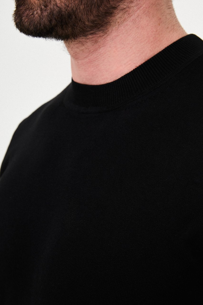 Men’s black cotton crewneck knit sweater styled with black trousers for fall winter fashion