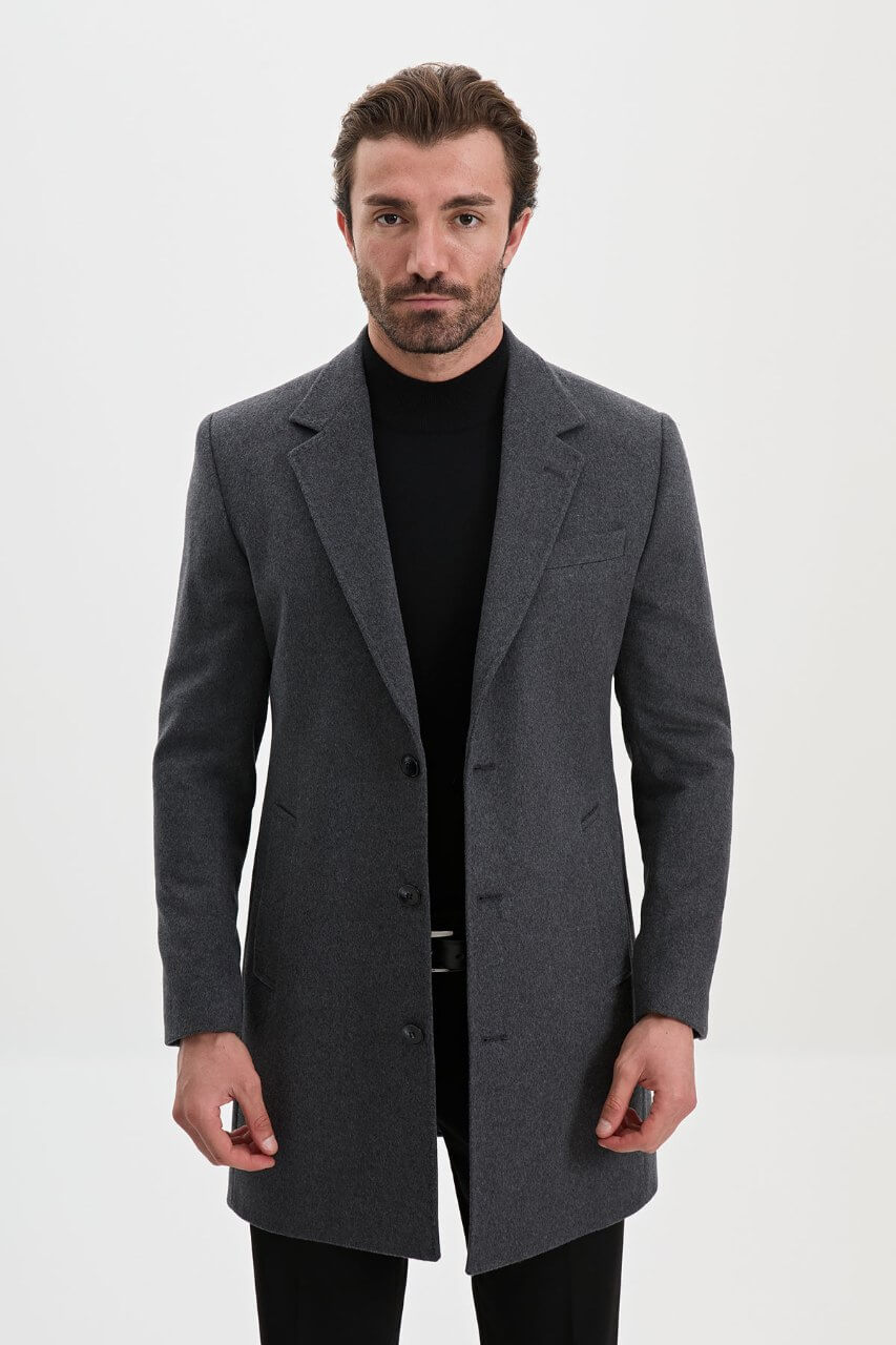 Men's dark grey single-breasted winter overcoat styled with a black roll-neck sweater and tailored trousers.