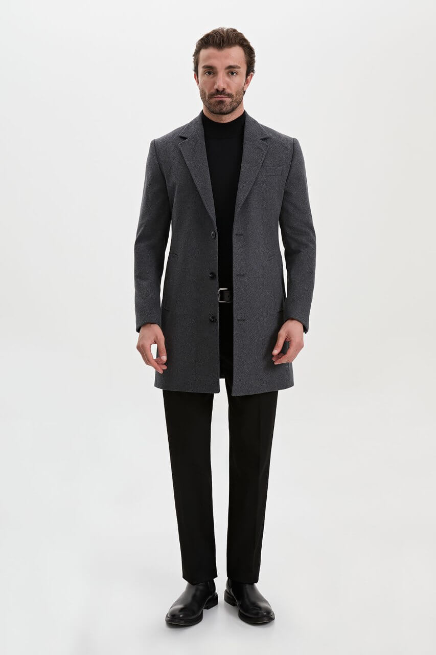 Men's dark grey single-breasted winter overcoat styled with a black roll-neck sweater and tailored trousers.