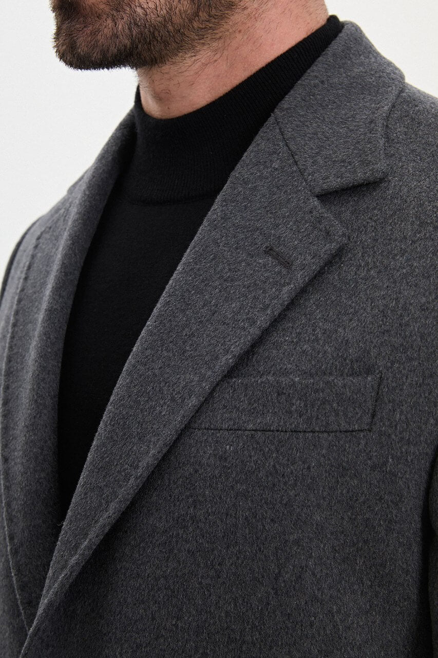 Men's dark grey single-breasted winter overcoat styled with a black roll-neck sweater and tailored trousers.