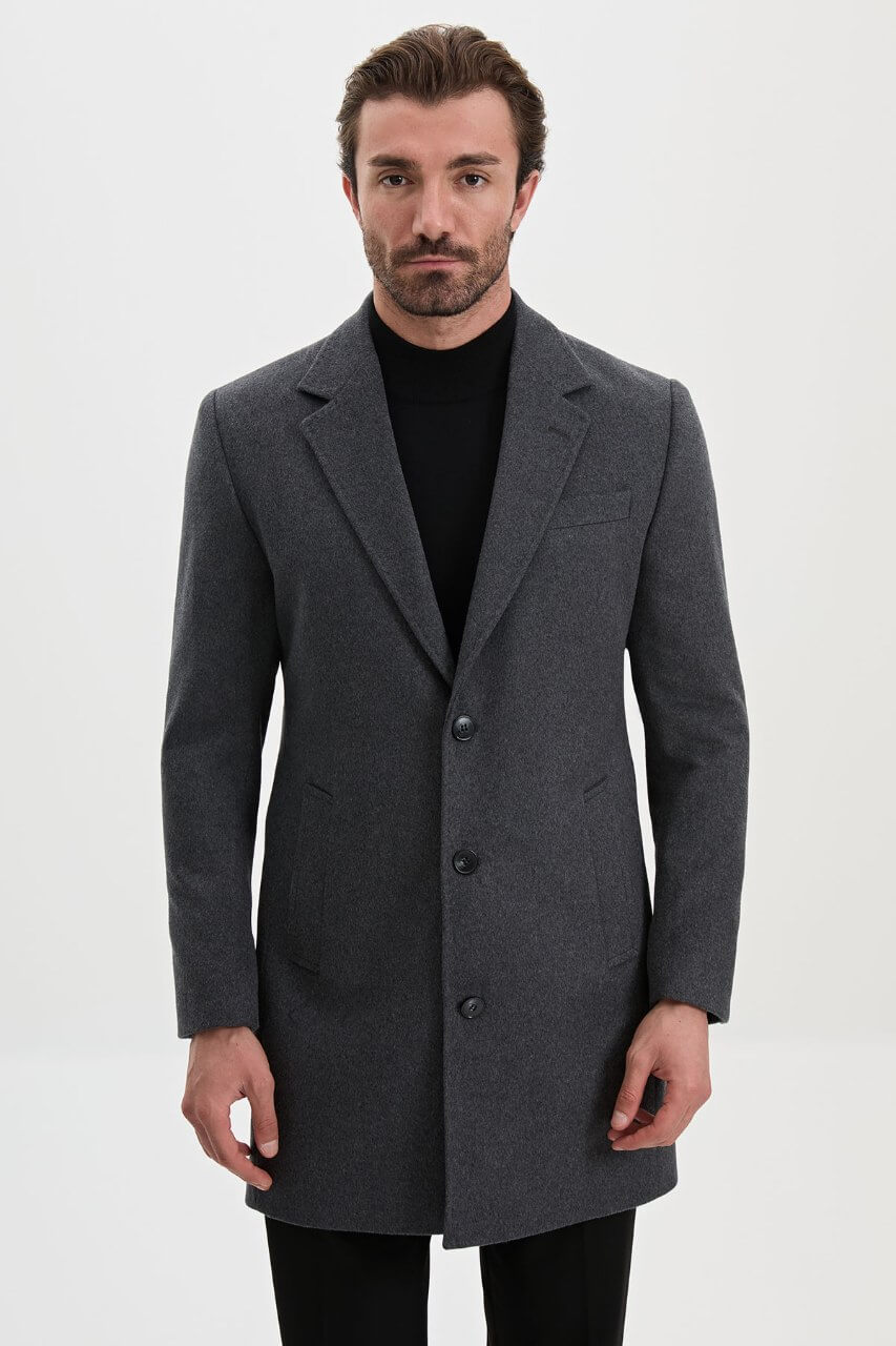 Men's dark grey single-breasted winter overcoat styled with a black roll-neck sweater and tailored trousers.
