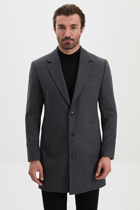 Men's dark grey single-breasted winter overcoat styled with a black roll-neck sweater and tailored trousers.