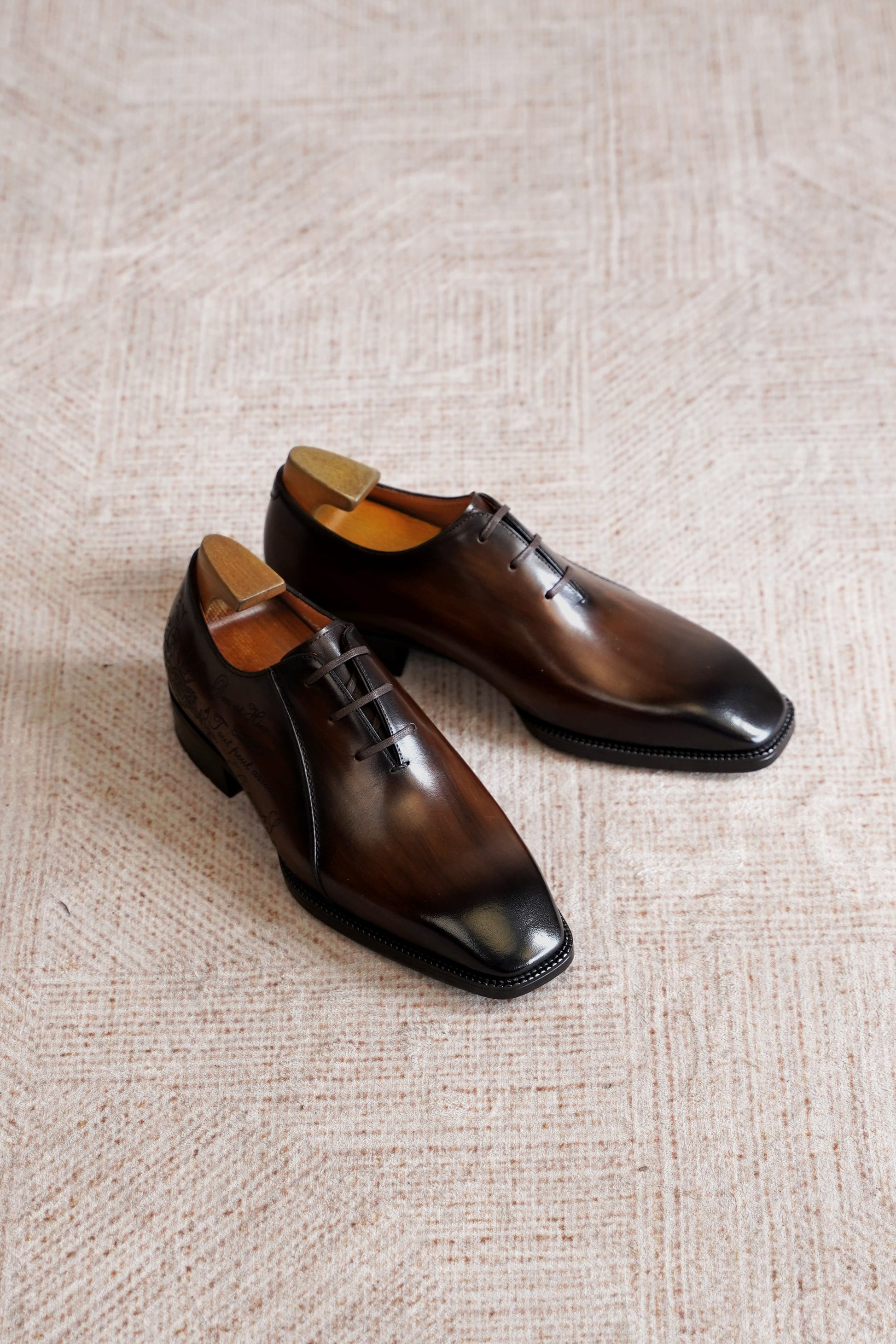 Men’s dark brown leather Oxford dress shoes with lace-up design, polished finish, pointed toe silhouette, and embossed script detail on the side panel.