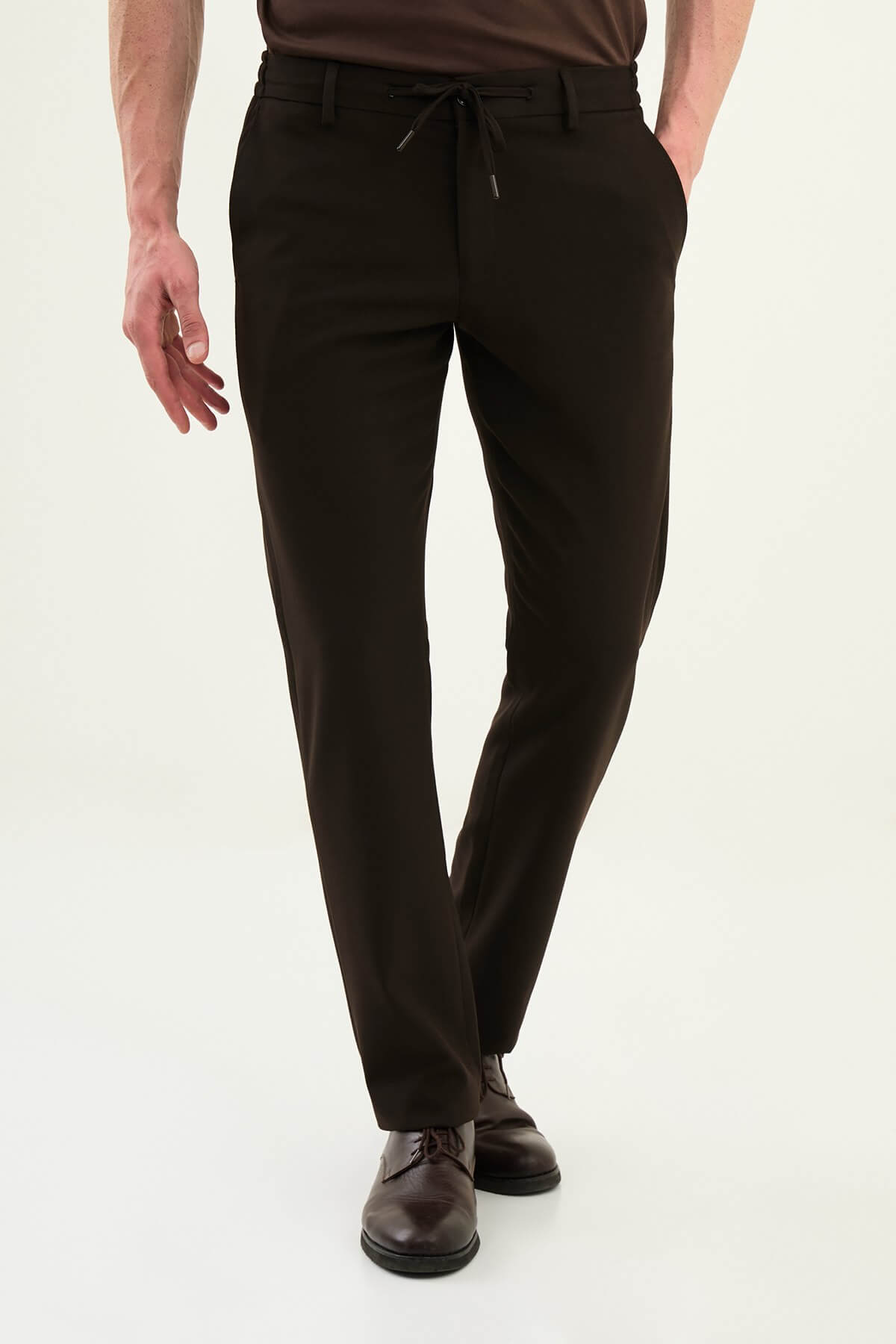 Men wearing dark brown slim-fit drawstring trousers with elastic waistband, casual-formal hybrid, styled with sneakers and dress shoes for versatile menswear.