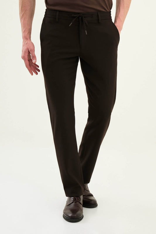 Men wearing dark brown slim-fit drawstring trousers with elastic waistband, casual-formal hybrid, styled with sneakers and dress shoes for versatile menswear.