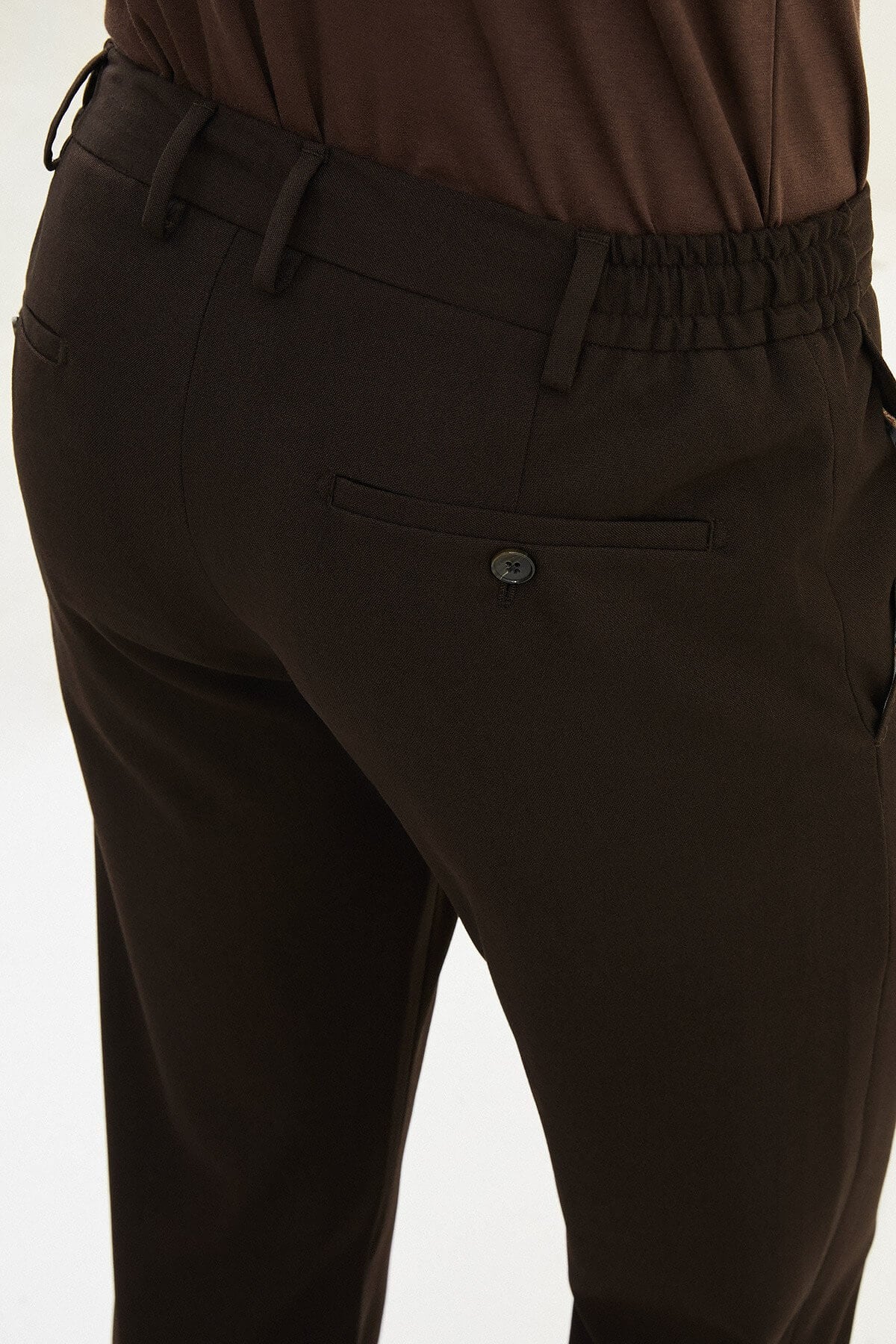 Men wearing dark brown slim-fit drawstring trousers with elastic waistband, casual-formal hybrid, styled with sneakers and dress shoes for versatile menswear.
