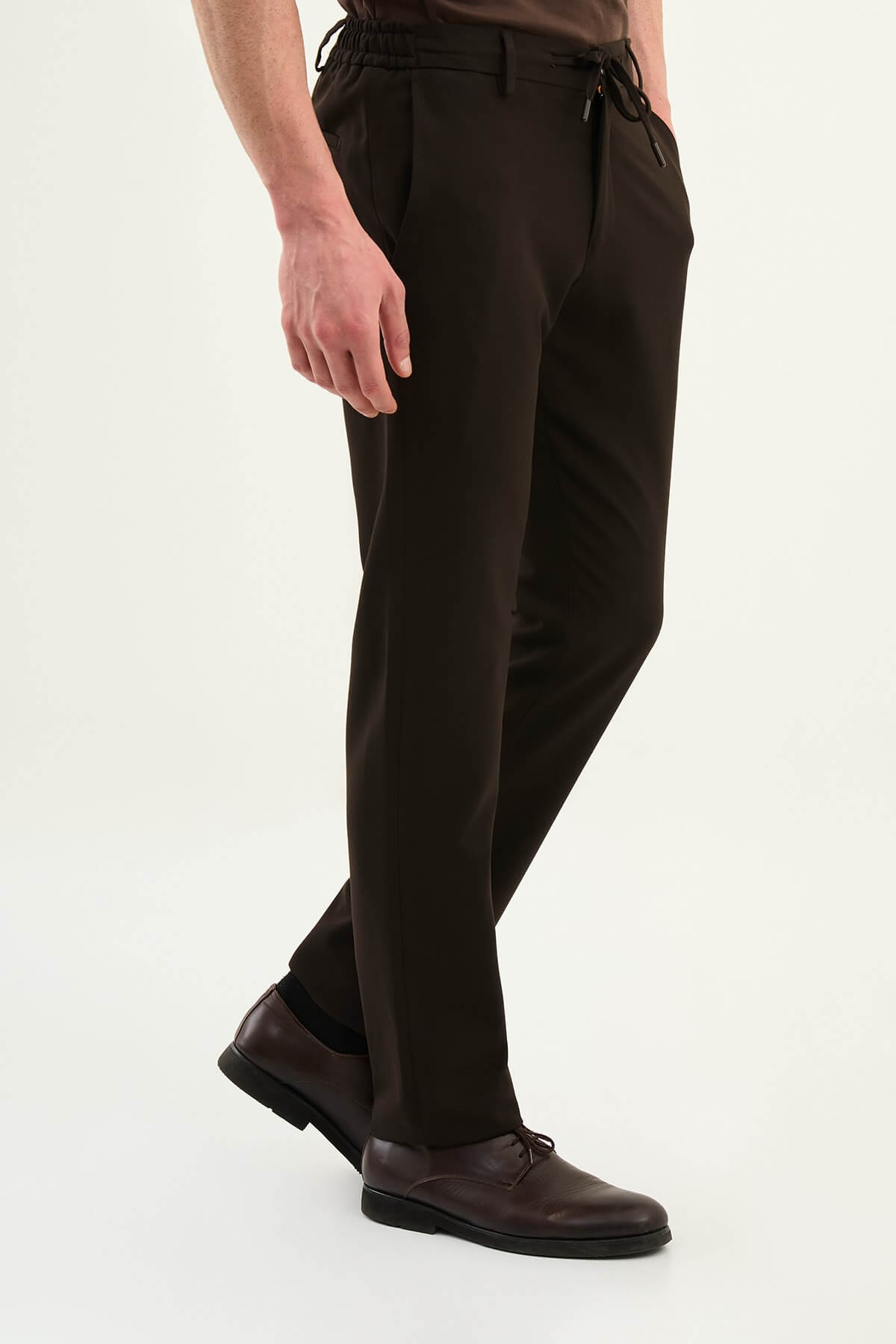 Men wearing dark brown slim-fit drawstring trousers with elastic waistband, casual-formal hybrid, styled with sneakers and dress shoes for versatile menswear.