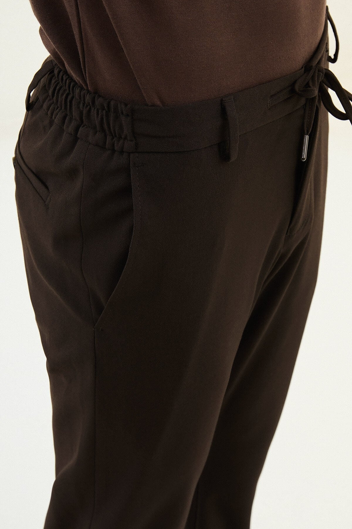Men wearing dark brown slim-fit drawstring trousers with elastic waistband, casual-formal hybrid, styled with sneakers and dress shoes for versatile menswear.