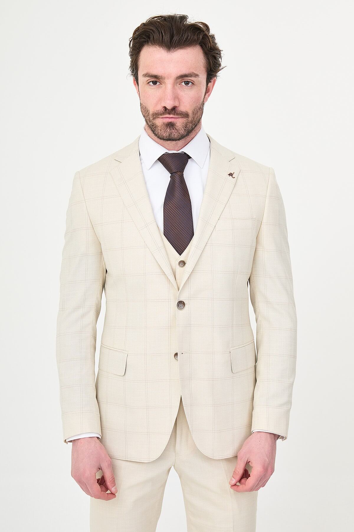 an ecru check slim-fit three-piece suit with matching waistcoat and trousers, white dress shirt, dark brown tie, and brown leather Derby shoes.