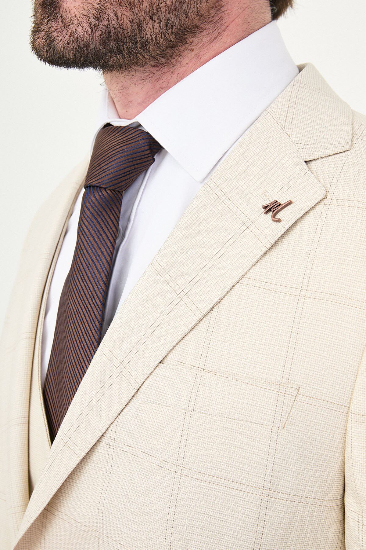 an ecru check slim-fit three-piece suit with matching waistcoat and trousers, white dress shirt, dark brown tie, and brown leather Derby shoes.