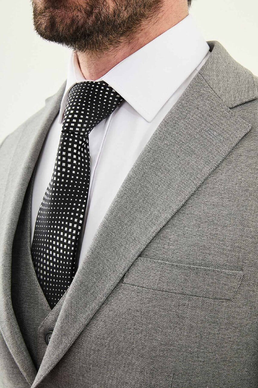 Man wearing a gray three-piece slim fit suit, including jacket, vest, and trousers, paired with a white dress shirt and black patterned tie